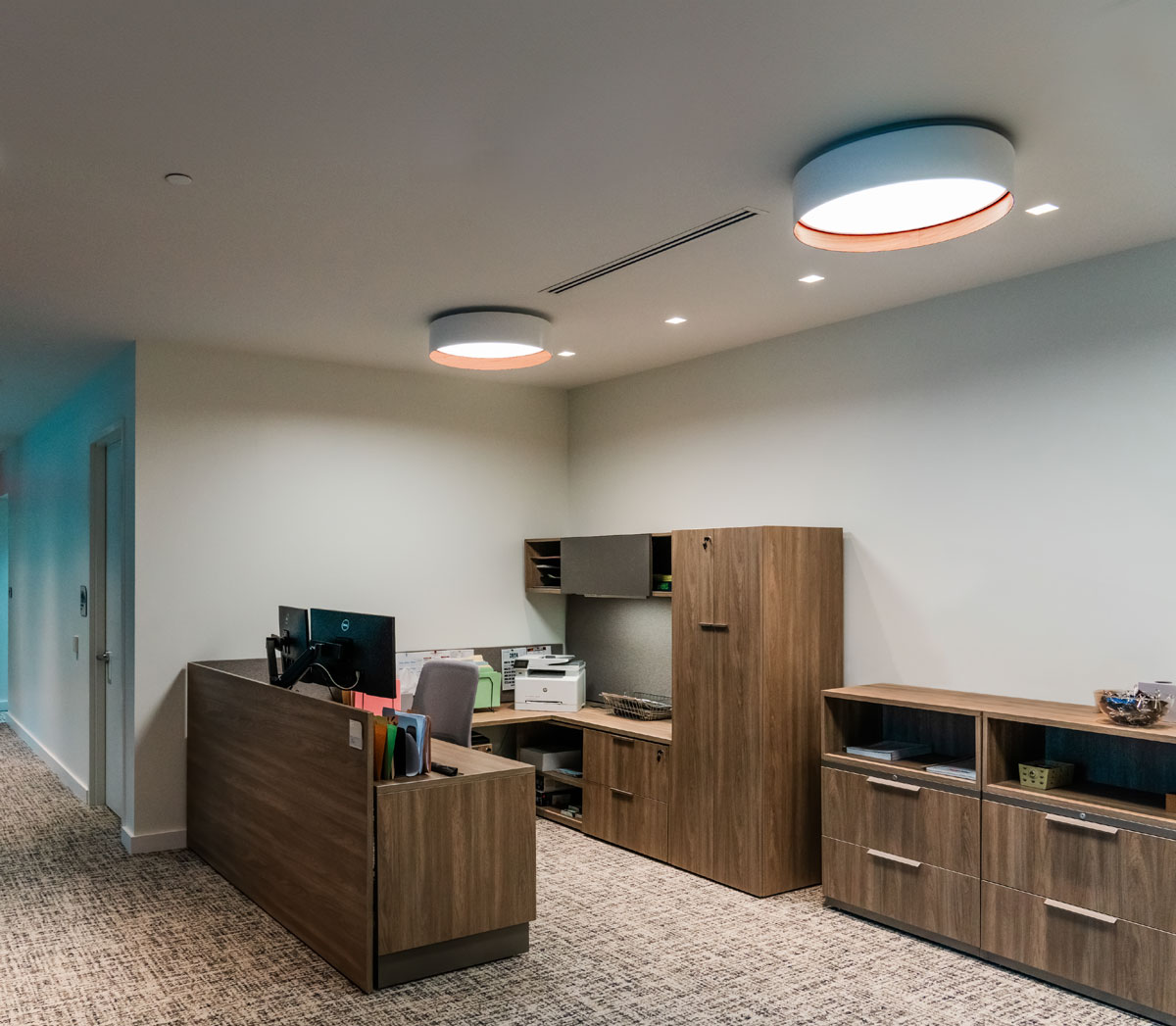 A workspace within Morgan Properties executive suite, illuminated by Muse pendant lighting in D61 MT White and D864 Walnut finish, providing soft, even illumination over each workstation.